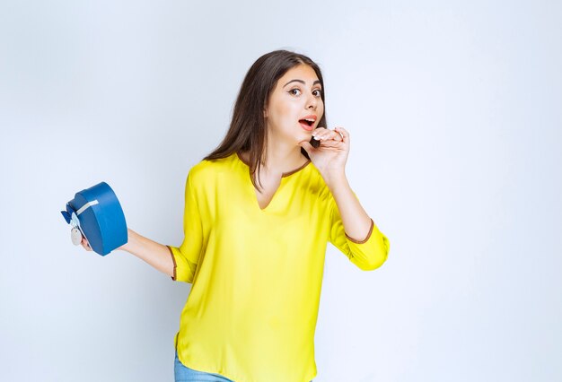 Girl holding a blue heart shape gift box and calling someone to present it.