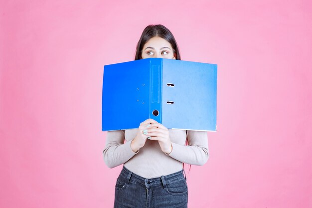 Free photo girl holding a blue project folder and hiding her face behind it