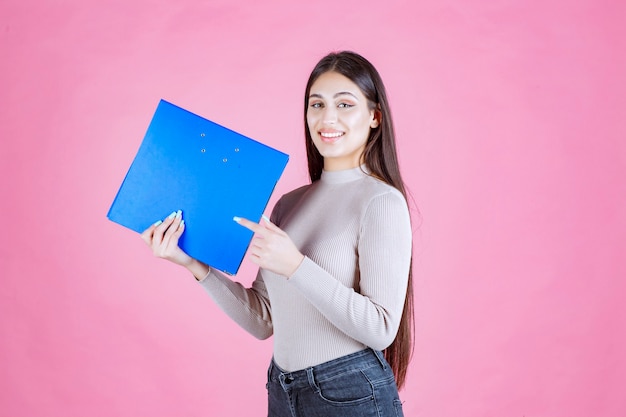 Девушка держит синюю папку проекта и выглядит успешной и счастливой