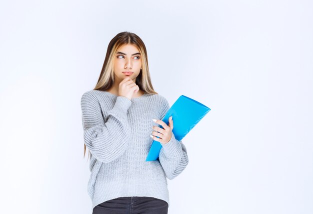 Girl holding a blue report folder and thinking.