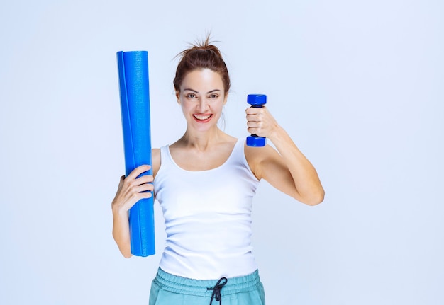 Девушка держит синий свернутый штейн для йоги и легкую гантель.