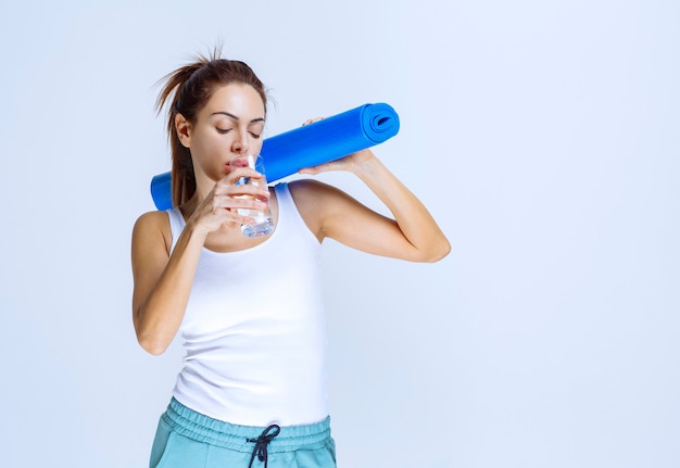 Девушка держит голубой штейн йоги и стакан воды.