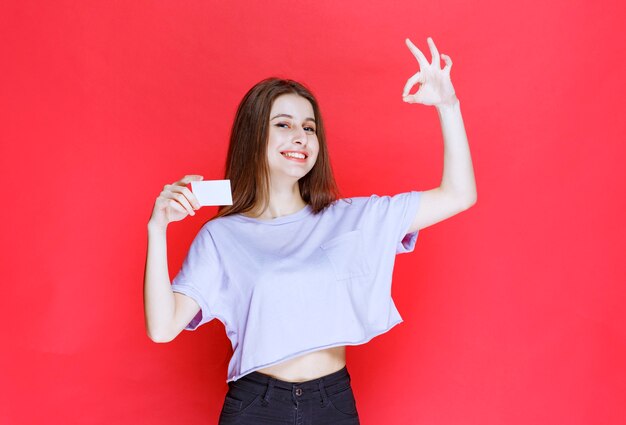 Girl holding a business card and showing positive hand sign. 