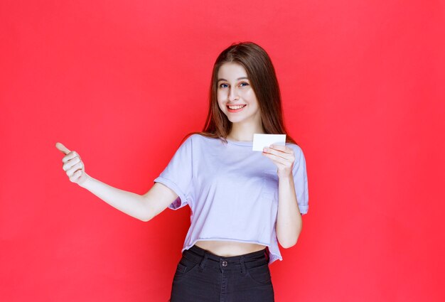 Girl holding a business card and showing positive hand sign. 