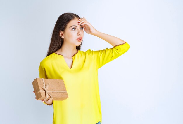 Girl holding a cardboard gift box and looks confised or thoughtful.