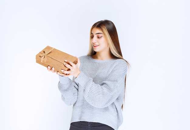 Free photo girl holding a cardboard gift box and looks surprized.