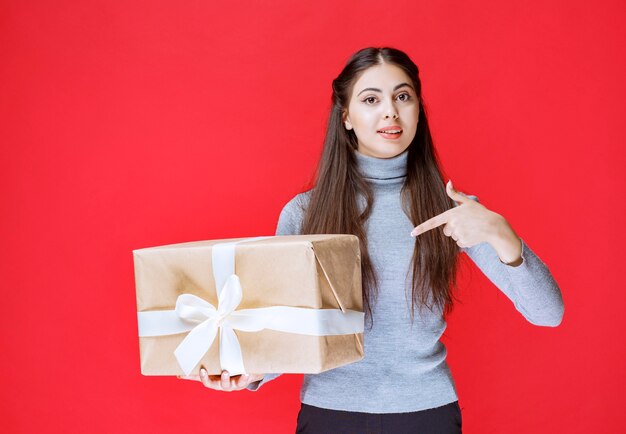 Girl holding a cardboard gift box and pointing at it.