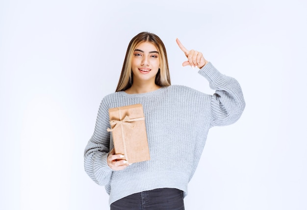 Girl holding a cardboard gift box and pointing a receiver aside.