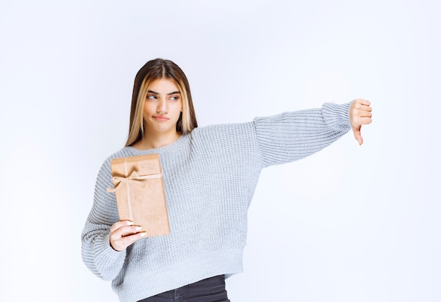 Girl holding a cardboard gift box and showing thumb down.