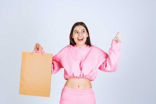 Girl holding a cardboard shopping bag and pointing above