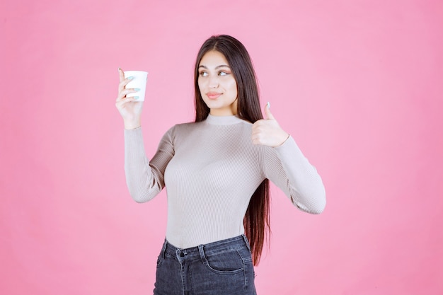 Ragazza che tiene una tazza di caffè e che mostra il pollice sul segno