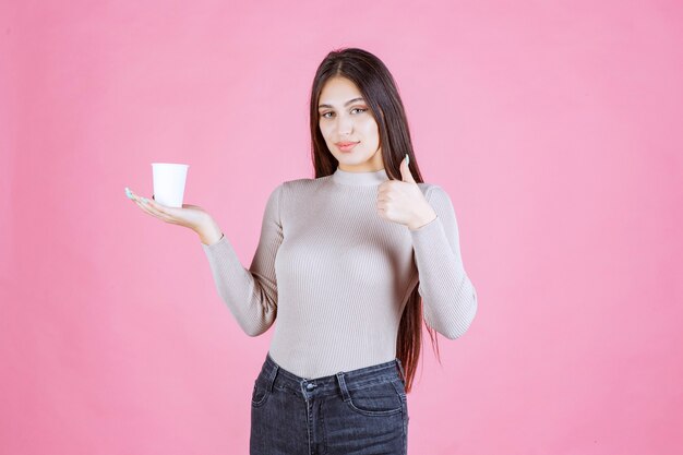 Girl holding a coffee cup and showing thumb up sign