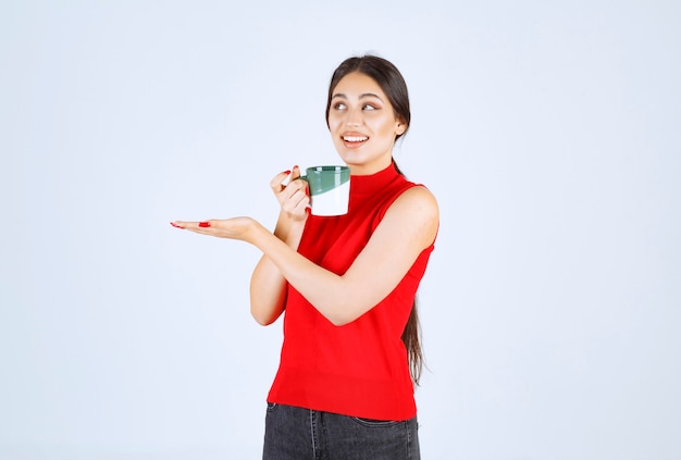 Girl holding a coffee mug and pointing to the left.