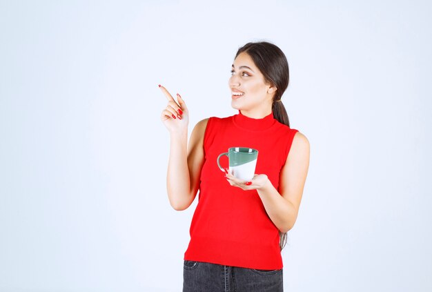 Girl holding a coffee mug and pointing to the left.