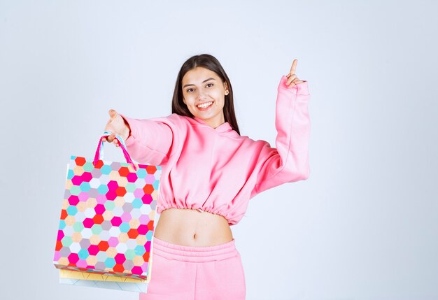 Girl holding colorful shopping bags and pointing at somewhere up. 