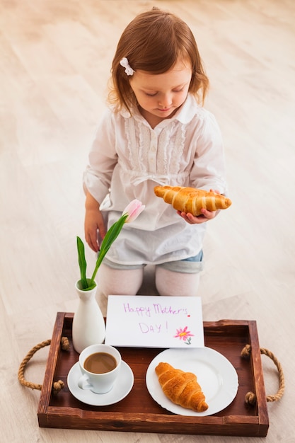 Free photo girl holding croissant near tray with greeting card