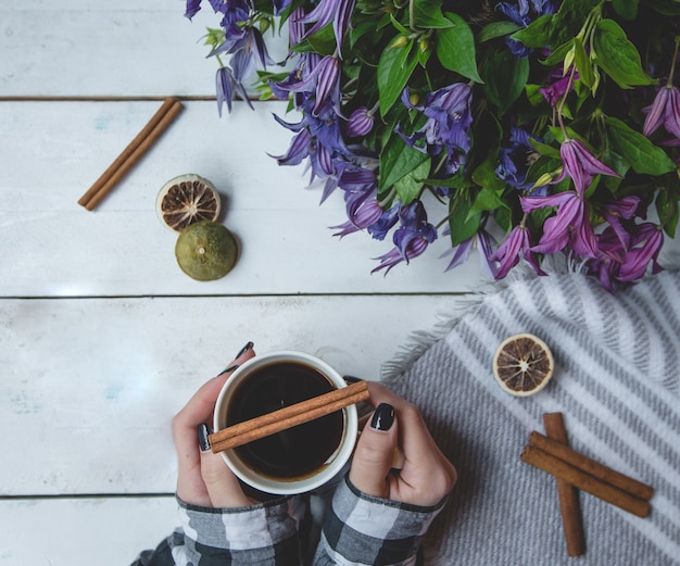 Girl holding a cup of tea with cinnamons and daisy bouquet standing aside