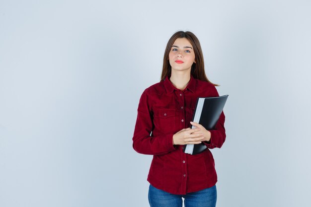 girl holding folder in burgundy shirt and looking intelligent.