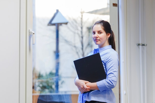 Girl holding folder standing against window