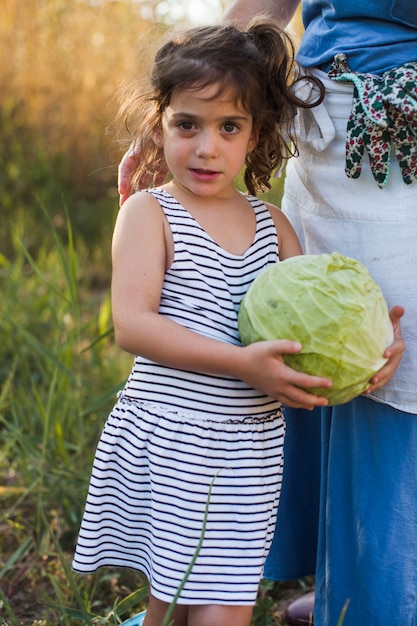 Girl holding fresh harvested cabbage standing with her mother