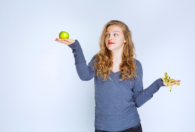 Girl holding a green apple in one hand and a measuring tape in another.