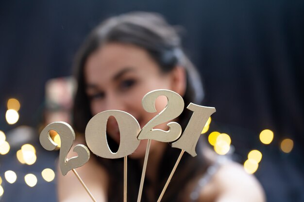 Girl holding in hand the number of the coming year on a dark blurred background.