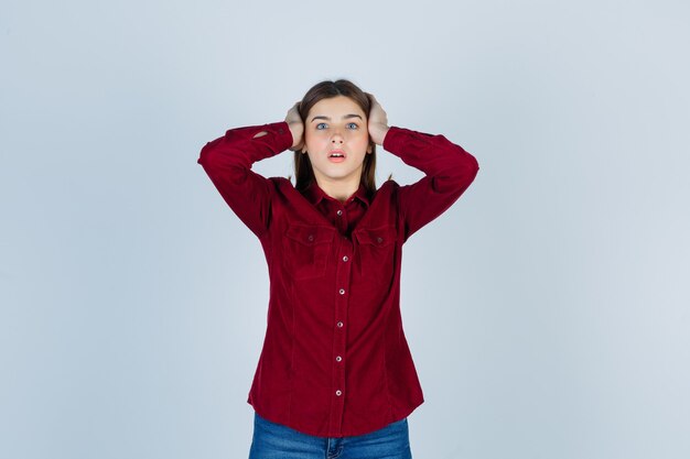 girl holding hands on head in burgundy shirt and looking excited.