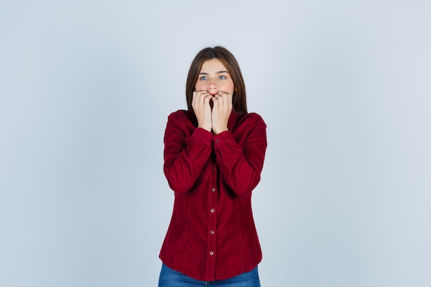 girl holding hands on mouth in casual shirt and looking frightened.