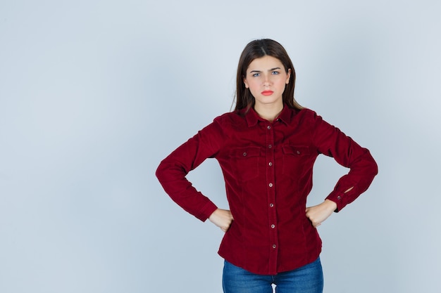 Free photo girl holding hands on waist in burgundy blouse and looking angry