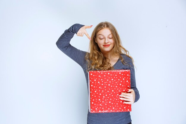 Free photo girl holding her red gift box and showing it.