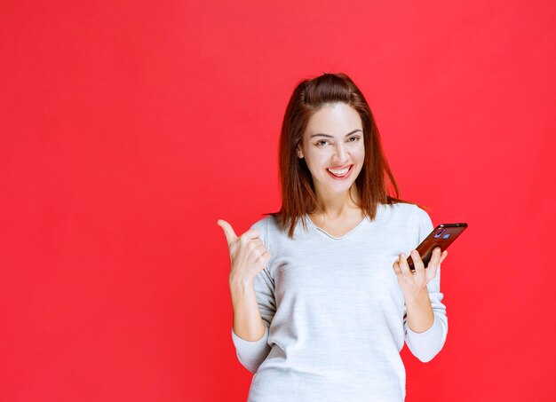 Girl holding a new model black smartphone and feeling positive and satisfied.