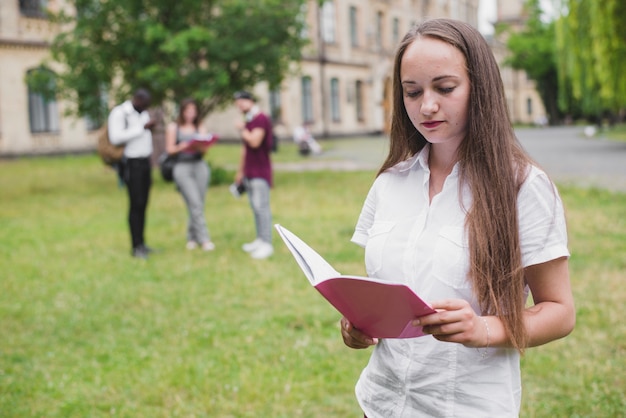 Free photo girl holding notebook reading standing outside