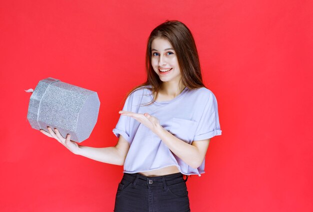 Girl holding and promoting a silver gift box . 
