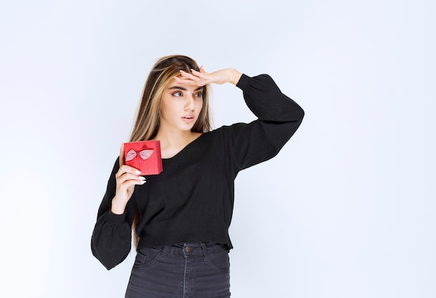 Girl holding a red gift box and noticing someone to come and receive it. High quality photo