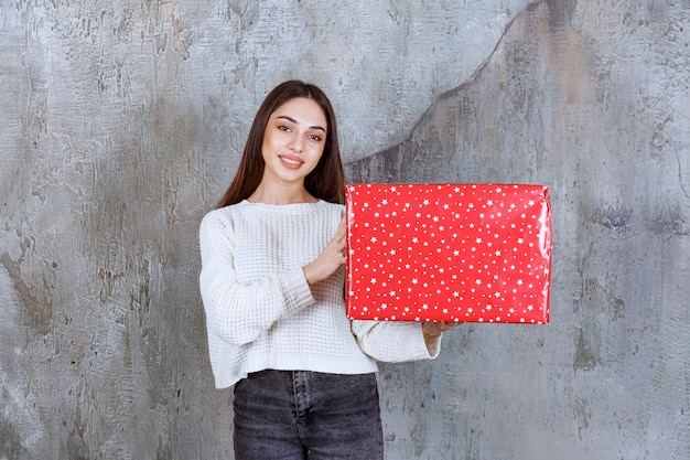 Girl holding a red gift box with white dots on it.