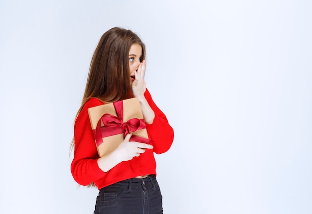 Girl holding a red ribbon wrapped cardboard gift box and looks stressed and terrified. 