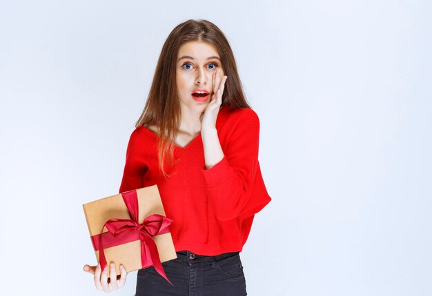Girl holding a red ribbon wrapped cardboard gift box and looks stressed and terrified. 