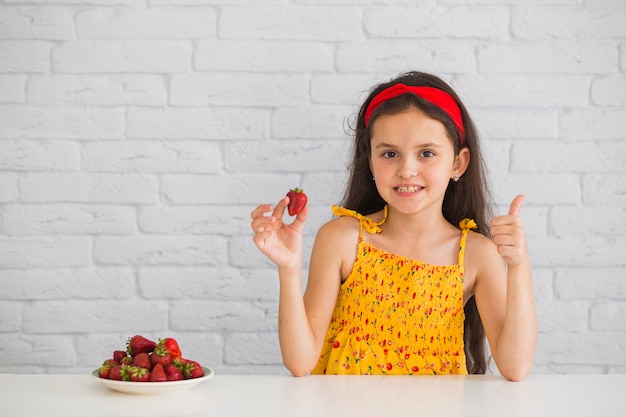 Girl holding red strawberry showing thumb up sign