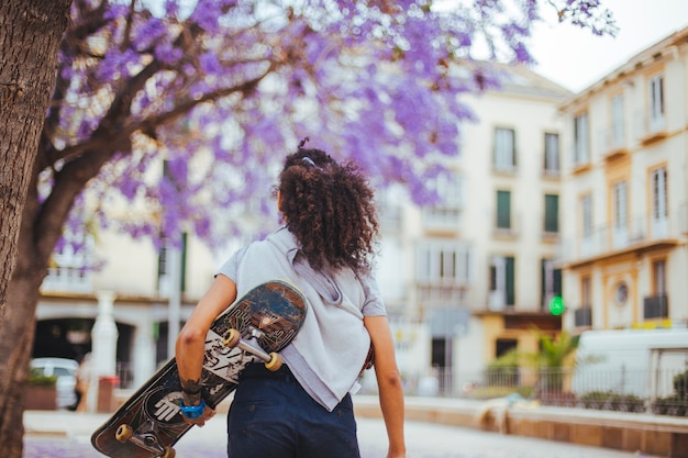 Girl holding skateboard walking under blooming trees