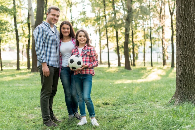 Girl holding soccer ball standing with her parent in park