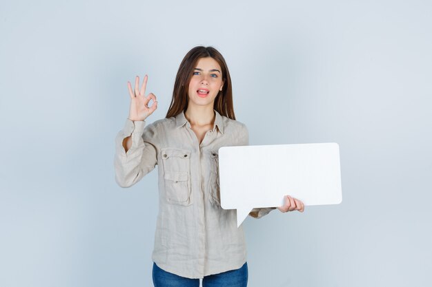 girl holding speech bubble, showing ok gesture in shirt and looking jolly.