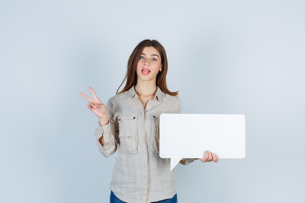 girl holding speech bubble, showing peace gesture in shirt and looking amazed.