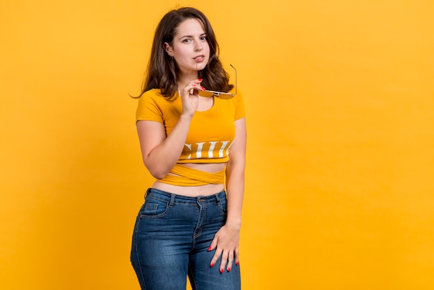 Girl holding sunglasses on yellow background