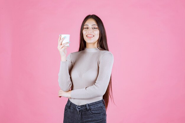 Girl holding a white disposable coffee cup, promoting it or smelling the fresh coffee