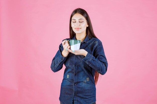 Girl holding a white green coffee mug and smelling