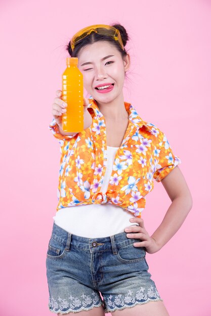 女の子はピンク色の背景にオレンジジュースの瓶を保持しています。