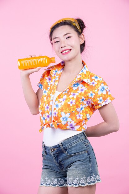 The girl holds a bottle of orange juice on a pink background.