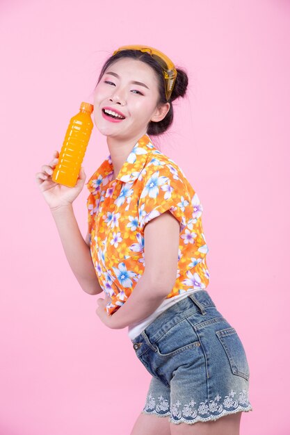 The girl holds a bottle of orange juice on a pink background.