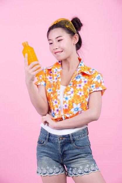 The girl holds a bottle of orange juice on a pink background.