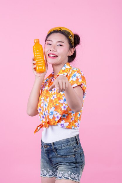 The girl holds a bottle of orange juice on a pink background.